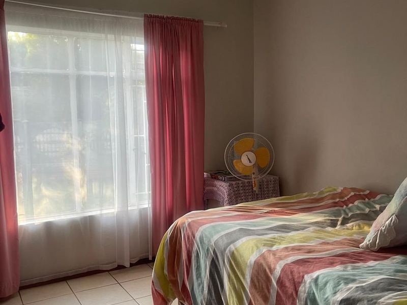 A bedroom featuring tiled flooring and a large window with curtain fittings, providing natural light.