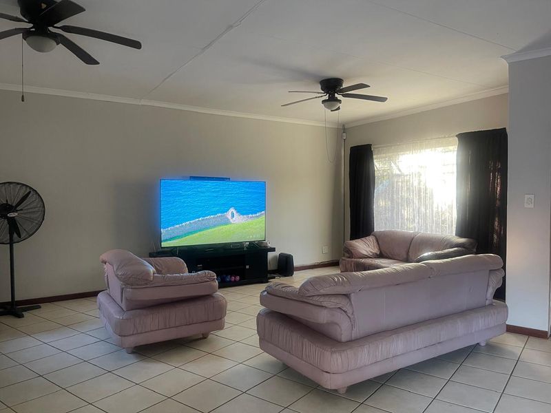 A spacious living room featuring tiled flooring and dual ceiling fans, providing a functional and comfortable area for relaxation.