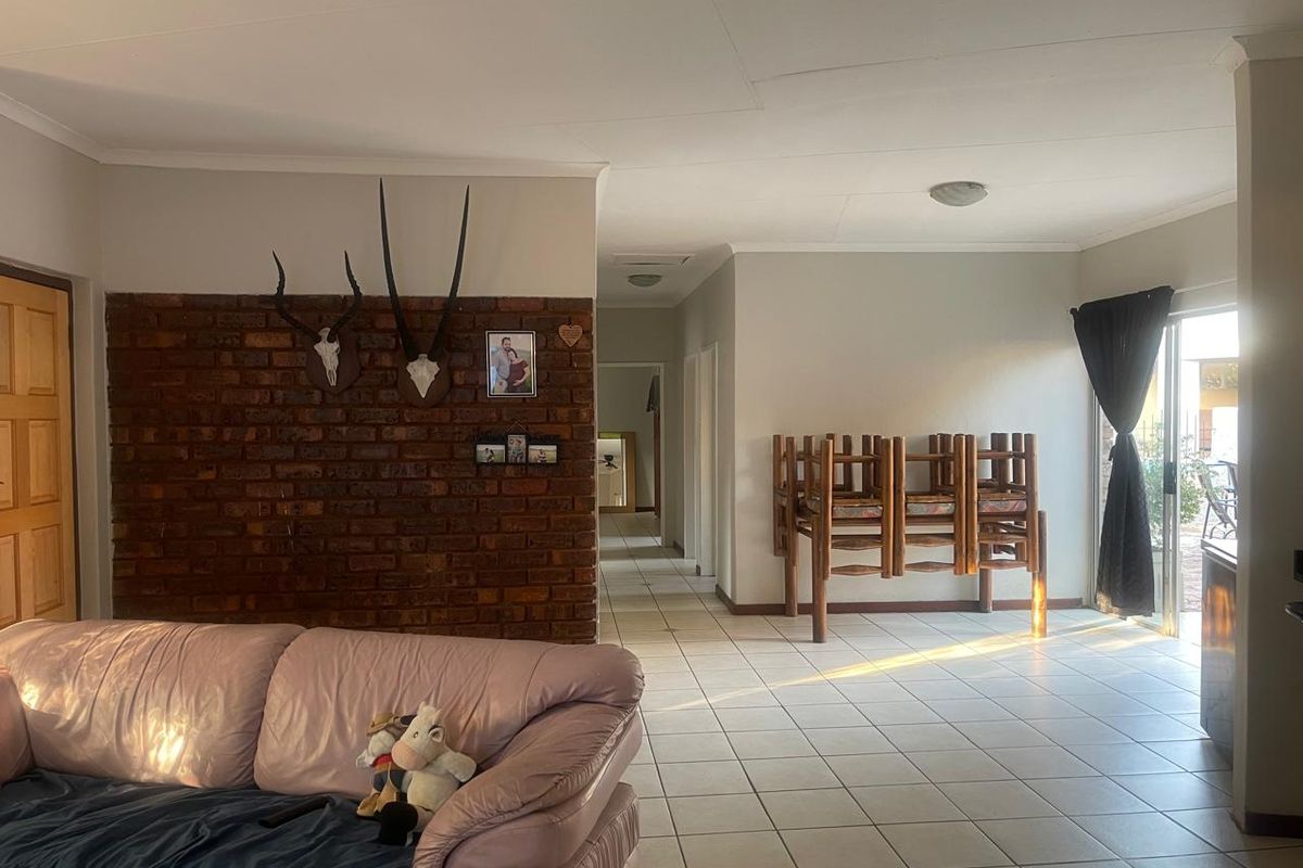 Spacious living area featuring an exposed brick accent wall, neutral ceramic floor tiles, and direct access to the outdoor area through a sliding glass door.