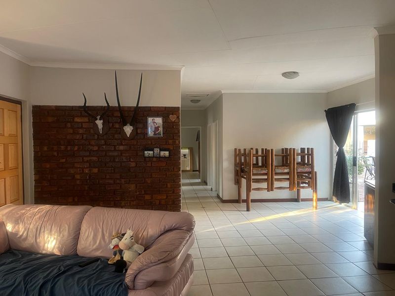 Spacious living area featuring an exposed brick accent wall, neutral ceramic floor tiles, and direct access to the outdoor area through a sliding glass door.