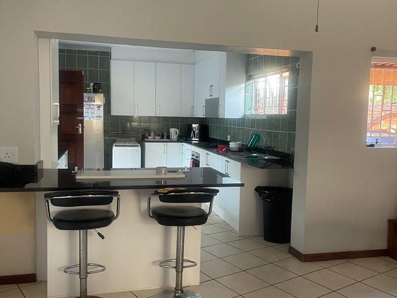 Open plan kitchen featuring a breakfast bar, granite countertops, and tiled flooring, seamlessly connected to the living area with a ceiling fan.