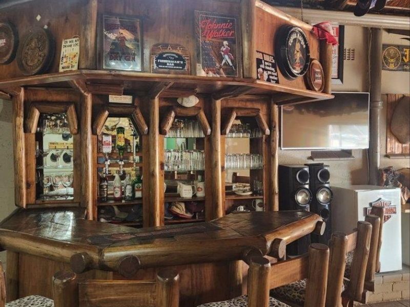 A rustic-style built-in timber bar area featuring a wooden counter, mirrored shelving, and a traditional thatch roof ceiling.