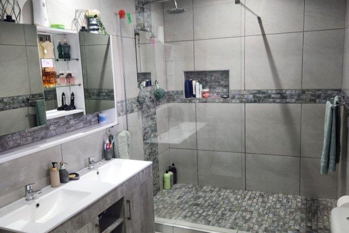 Modern bathroom featuring a double vanity with storage, a spacious walk-in shower with a glass screen, and contemporary grey tiled finishes.