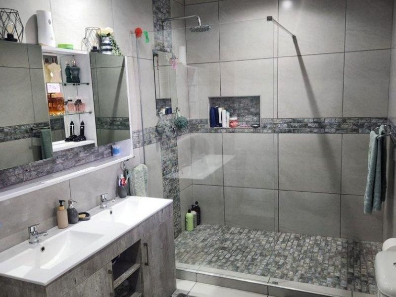 Modern bathroom featuring a double vanity with storage, a spacious walk-in shower with a glass screen, and contemporary grey tiled finishes.