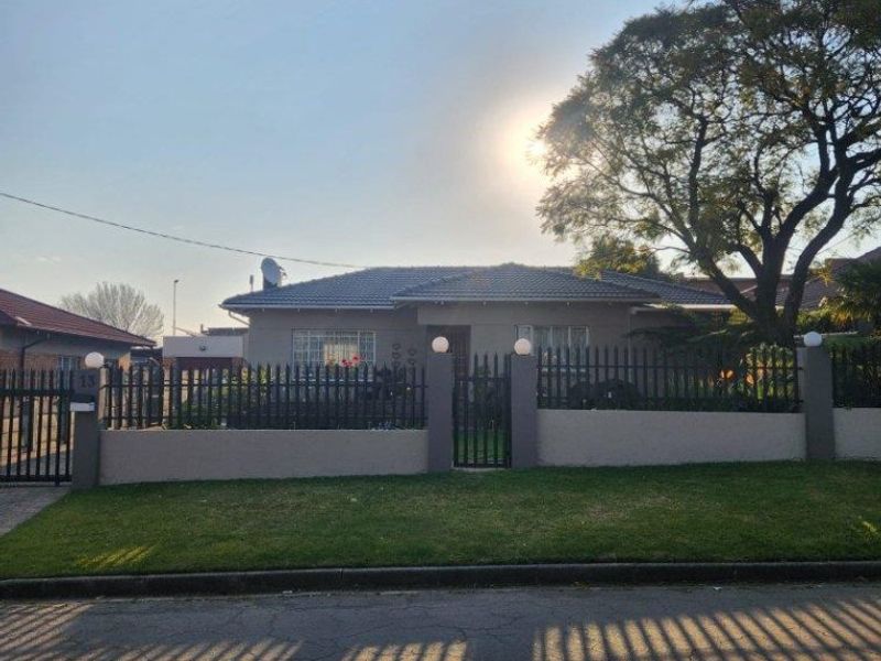 Front elevation of a single-story house featuring a perimeter wall, metal security fencing, and a gated entrance with a well-maintained front lawn.