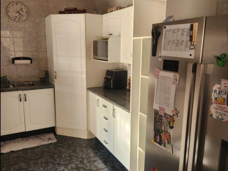 A functional kitchen featuring white cabinetry, laminate countertops, a stainless steel sink, and tiled finishes throughout.