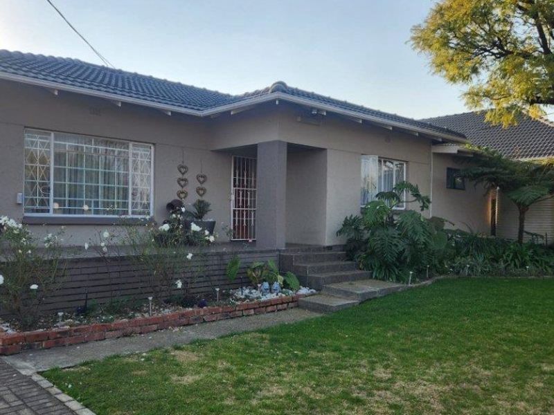 Front elevation of a single-story house featuring a tiled roof, security entrance gate, and a brick-retained garden bed with a paved driveway.