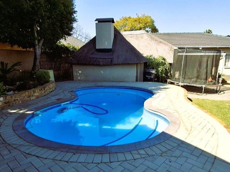 Outdoor entertainment area featuring a swimming pool, paved surround, and a traditional thatched lapa structure in the rear garden.