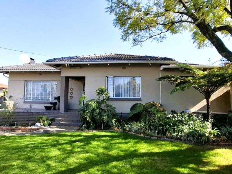 Front elevation of a single-story house featuring a tiled roof, concrete porch, and established garden with mature trees.