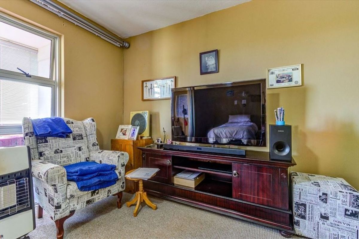 A bedroom featuring carpet flooring and a window, currently utilized as a living space with a television console.