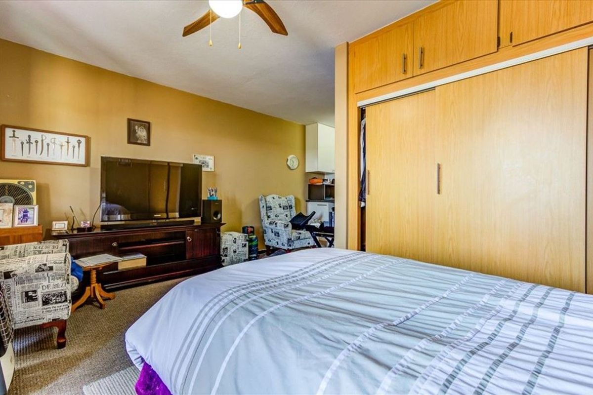A bedroom featuring built-in wooden cupboards and a ceiling fan, offering functional storage space.