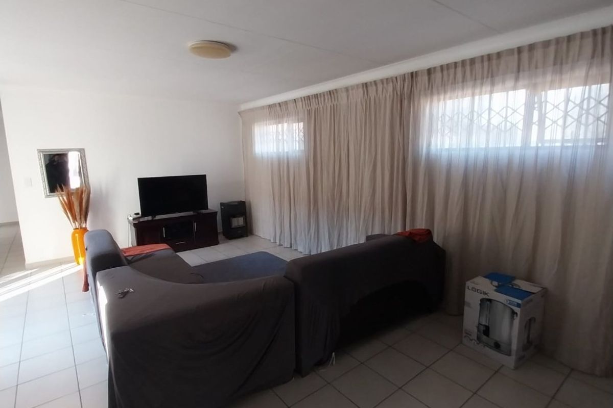 A living room featuring tiled flooring and large windows covered by curtains with integrated security gates.