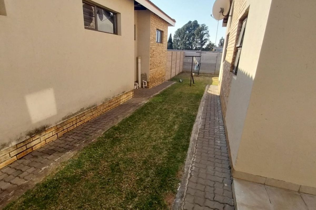 A side garden area featuring a paved walkway between two townhouse structures with a small lawn and boundary wall.