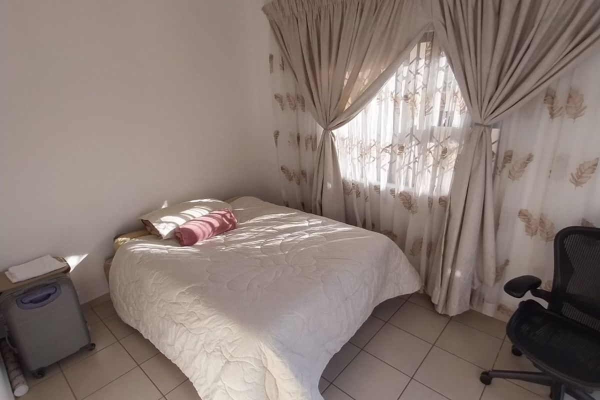 A functional bedroom featuring tiled flooring and a window fitted with a security gate and curtains.
