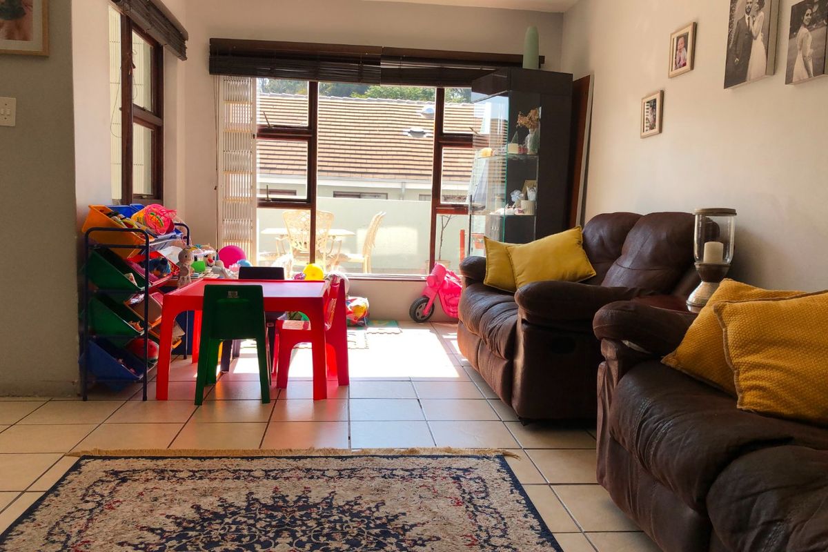 A living room featuring tiled flooring and large windows that provide natural light and access to an outdoor area.