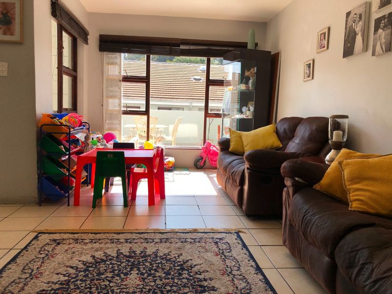 A living room featuring tiled flooring and large windows that provide natural light and access to an outdoor area.