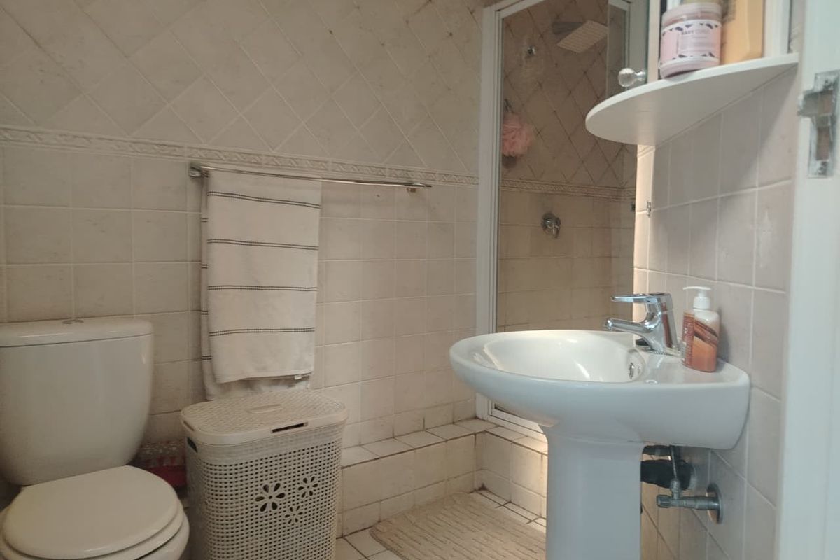 A compact bathroom featuring a pedestal basin, toilet, and a separate shower enclosure with tiled walls and flooring.