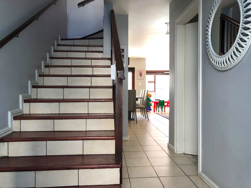 Entrance hallway featuring a tiled staircase with a wooden handrail, leading through to an open-plan living and dining area.