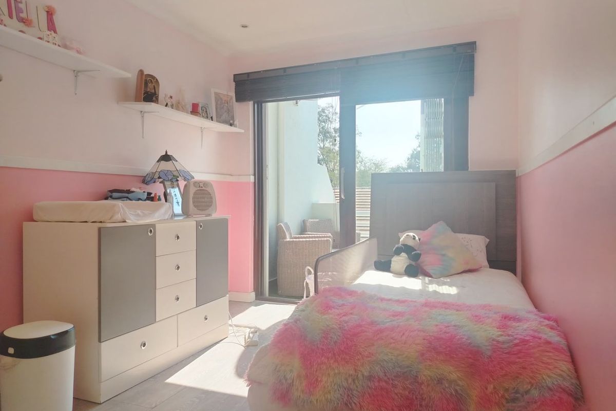 A bright bedroom featuring laminate flooring, recessed lighting, and a sliding glass door providing access to an outdoor balcony area.
