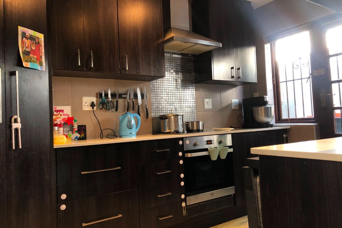 A functional kitchen featuring dark wood cabinetry, a stainless steel extractor fan, mosaic tile splashback, and built-in oven with hob.