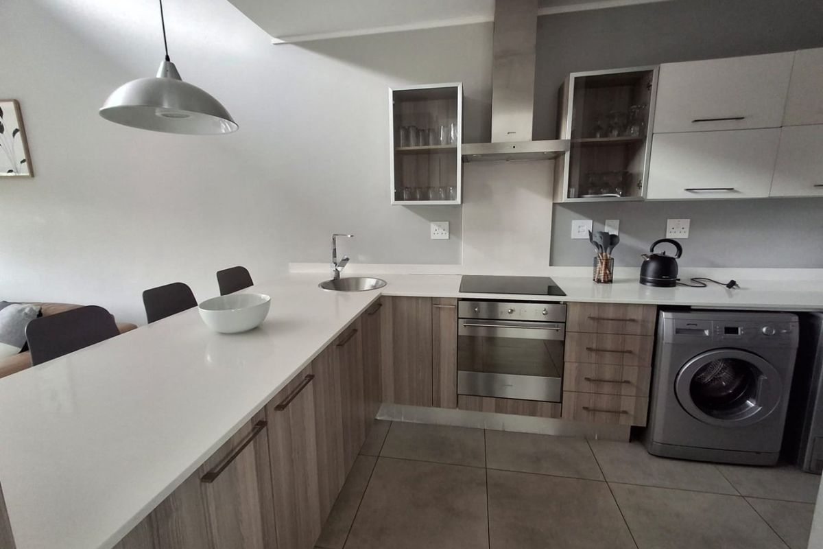 Modern kitchen featuring wood-finish cabinetry, stone countertops, integrated oven and hob, and a breakfast bar, complemented by neutral tiled flooring.