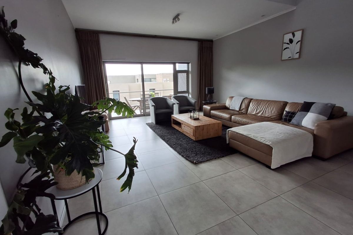 Spacious living room featuring large format floor tiles, neutral walls, and a wide sliding glass door providing access to an outdoor balcony area.