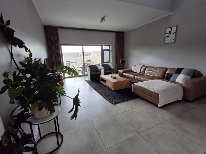 Spacious living room featuring large format floor tiles, neutral walls, and a wide sliding glass door providing access to an outdoor balcony area.