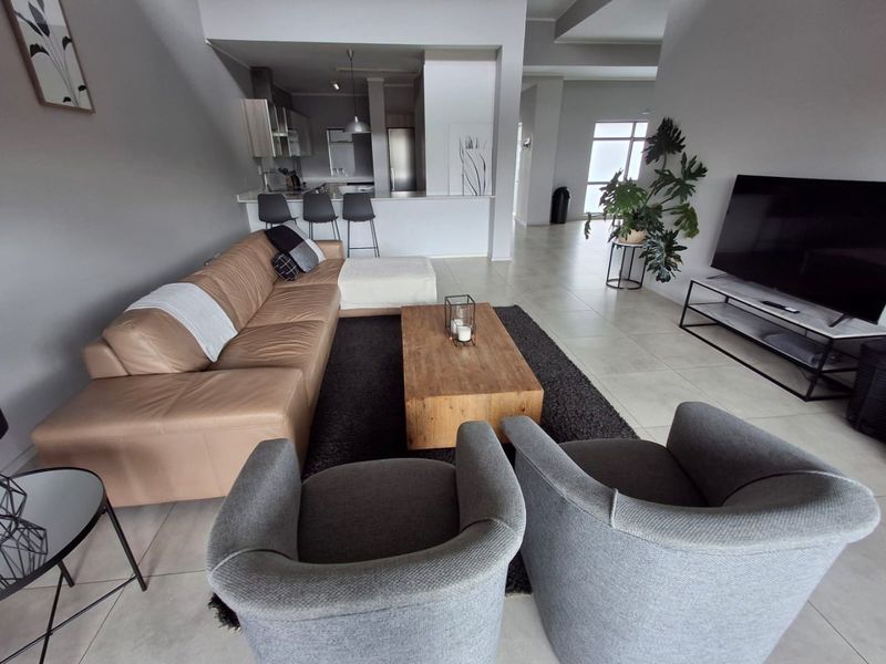 Spacious open-plan living area featuring tiled floors and a modern kitchen with a breakfast bar, creating a seamless flow for entertaining.