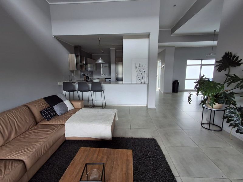 Spacious open-plan living area featuring a modern kitchen with a breakfast bar, neutral tiled flooring, and a seamless flow into the lounge space.