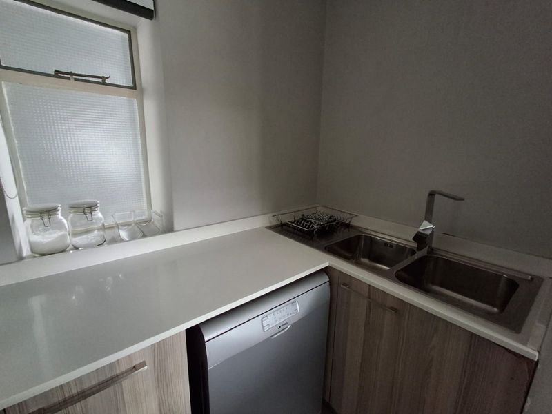 A functional scullery area featuring a double stainless steel sink, stone countertops, and modern laminate cabinetry with an integrated dishwasher.