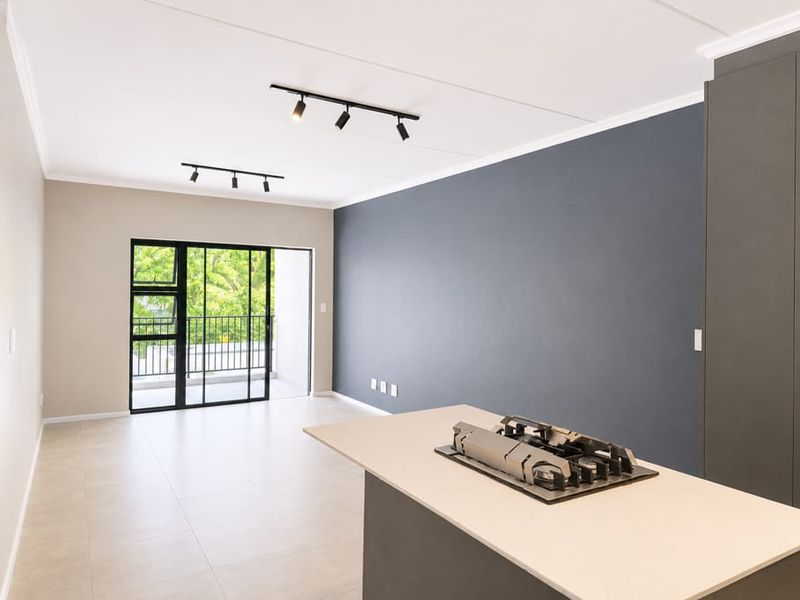 Modern open-plan living area featuring a kitchen island with a built-in gas cooktop, sleek cabinetry, track lighting, and access to a private balcony.