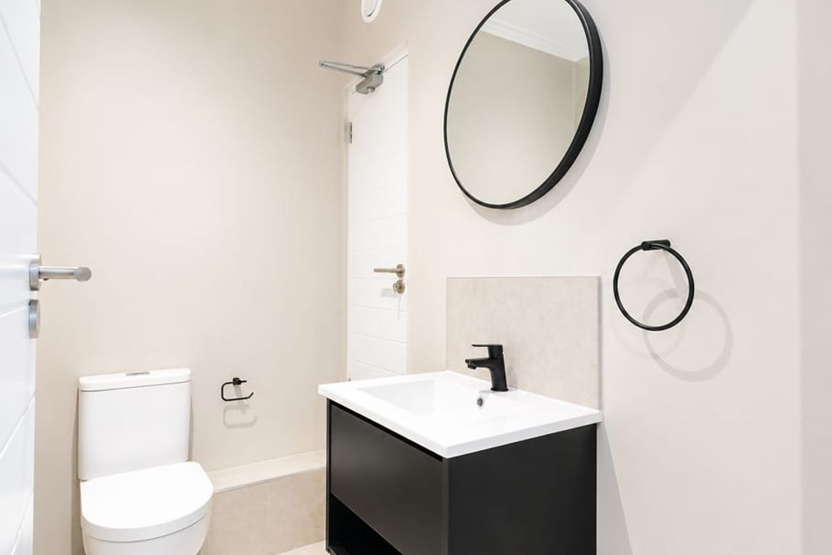 A modern, minimalist bathroom featuring a sleek black vanity, basin with black mixer tap, and a contemporary circular mirror.