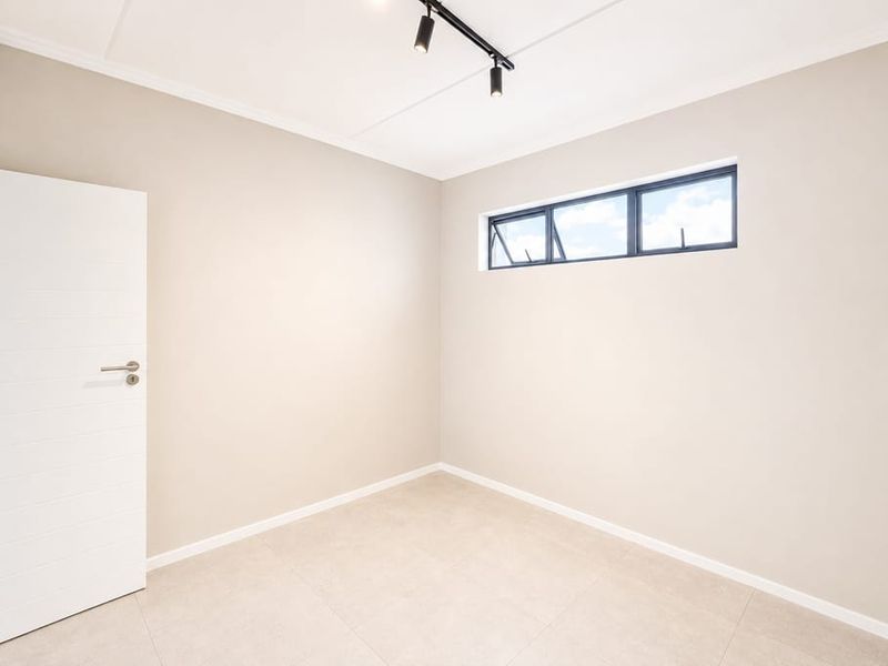 A bright, neutral-toned bedroom featuring modern tiled flooring, track lighting, and a horizontal window, presented in excellent, move-in ready condition.