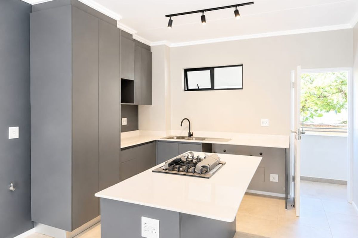 Modern kitchen featuring sleek grey cabinetry, stone countertops, a central island with a gas hob, and contemporary track lighting.