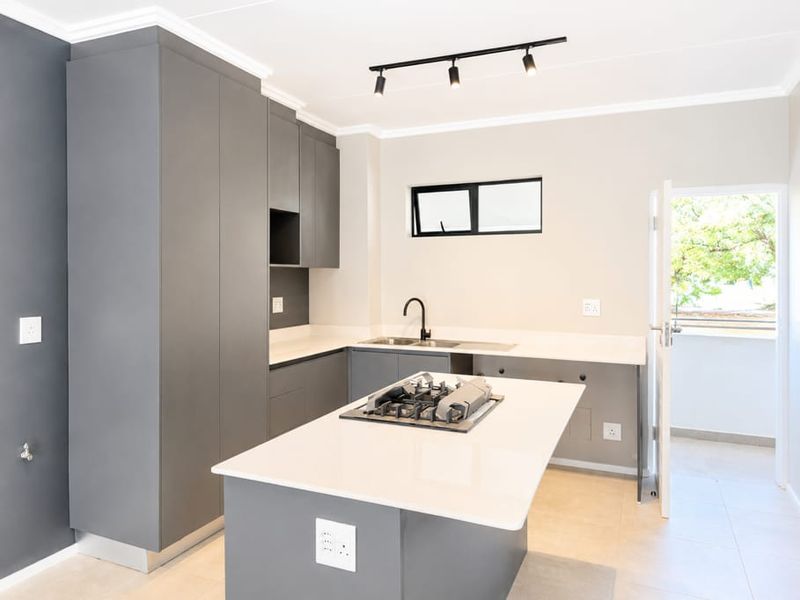 Modern kitchen featuring sleek grey cabinetry, stone countertops, a central island with a gas hob, and contemporary track lighting.