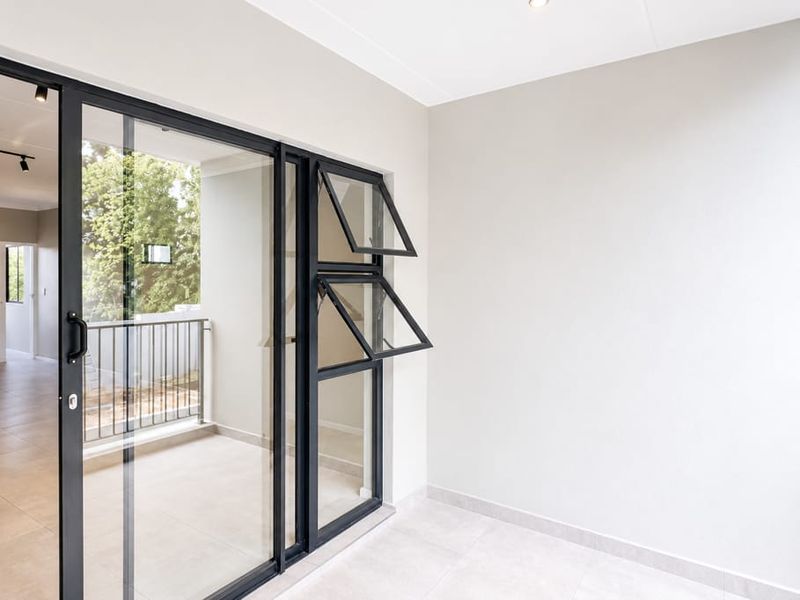 A clean, modern covered balcony featuring tiled flooring, large sliding glass doors, and a metal balustrade, offering a bright and neutral outdoor space.