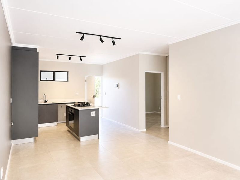 Modern open-plan kitchen featuring dark cabinetry, a central island with a gas hob, and neutral tiled flooring in a bright, spacious living area.