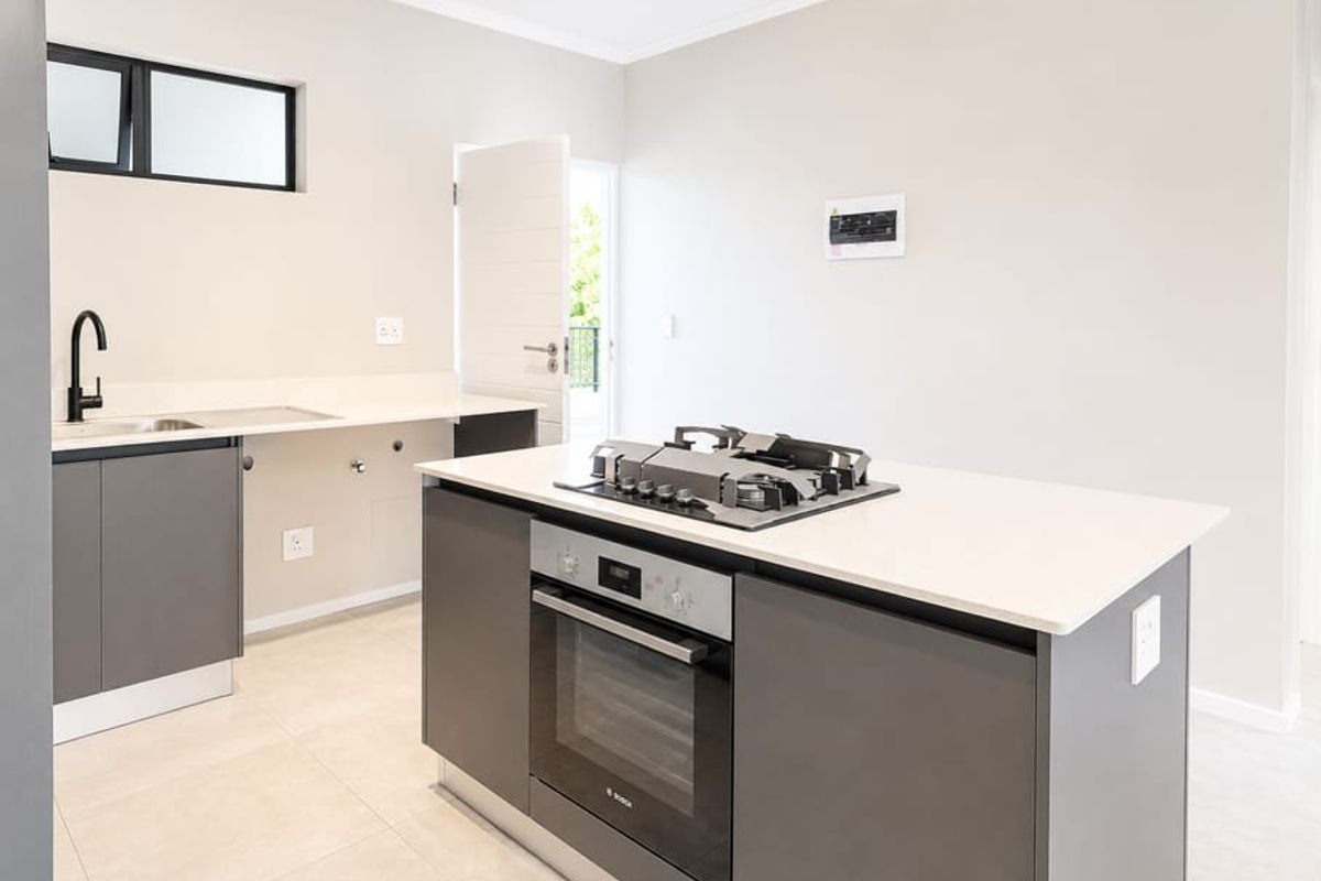 Modern kitchen featuring a central island with a built-in oven and gas hob, stone countertops, and sleek cabinetry in a neutral, well-lit space.