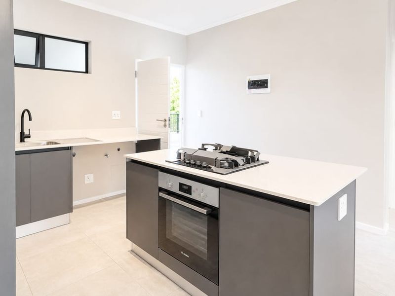 Modern kitchen featuring a central island with a built-in oven and gas hob, stone countertops, and sleek cabinetry in a neutral, well-lit space.