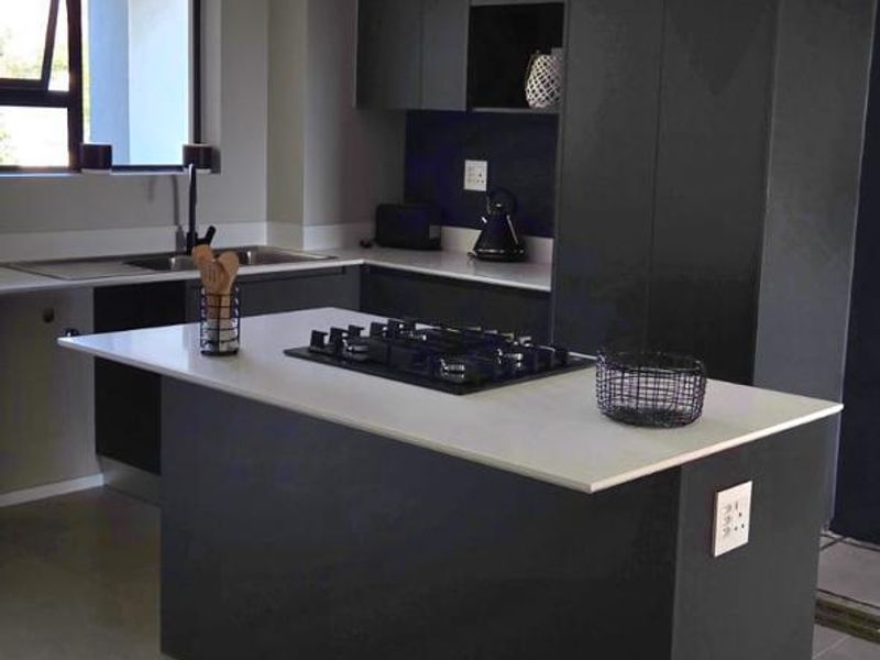 Modern kitchen featuring dark cabinetry, a central island with a built-in hob, quartz countertops, and sleek track lighting.
