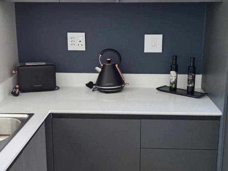 Modern kitchen area featuring sleek dark grey cabinetry, white stone countertops, and neutral floor tiles.