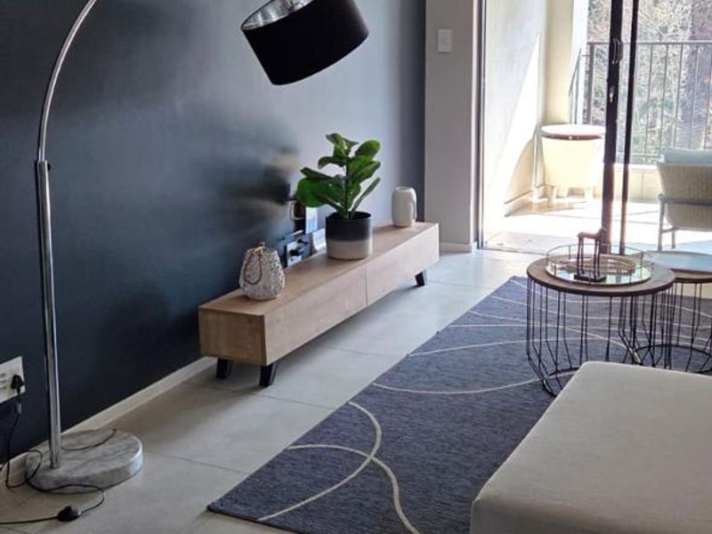 Modern living room featuring large format floor tiles, a dark accent wall, and sliding glass doors providing access to an outdoor balcony area.