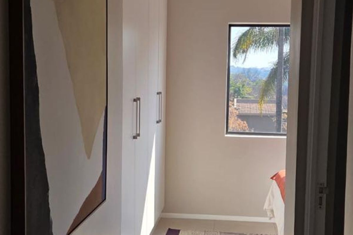 A well-lit bedroom featuring built-in cupboards, neutral tiled flooring, and a window providing natural light and exterior views.