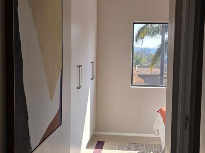 A well-lit bedroom featuring built-in cupboards, neutral tiled flooring, and a window providing natural light and exterior views.