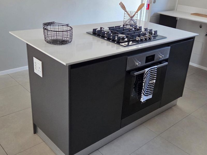 Modern kitchen island featuring a sleek stone countertop, integrated gas cooktop, and built-in oven, set against neutral tiled flooring.