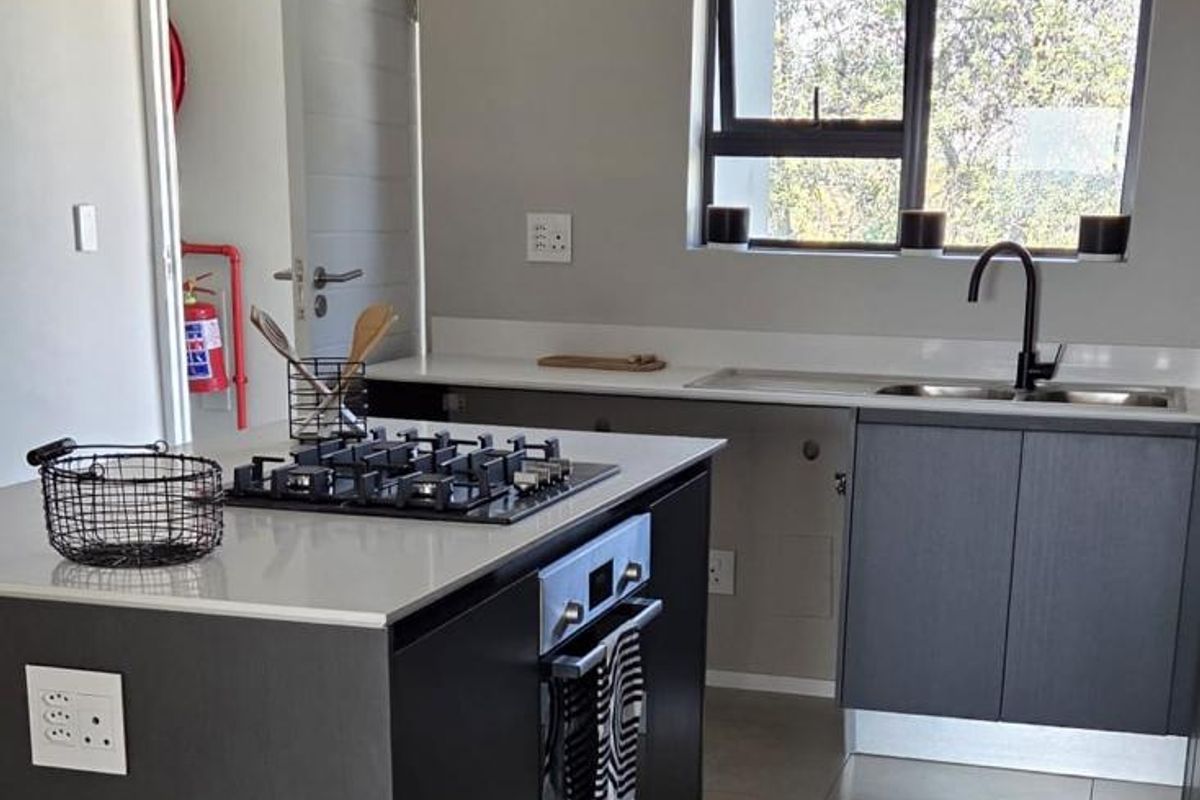 Modern kitchen featuring a central island with a gas hob and built-in oven, complemented by sleek cabinetry, quartz countertops, and contemporary track lighting.