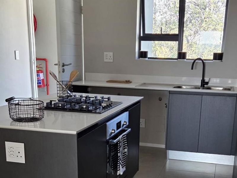 Modern kitchen featuring a central island with a gas hob and built-in oven, complemented by sleek cabinetry, quartz countertops, and contemporary track lighting.