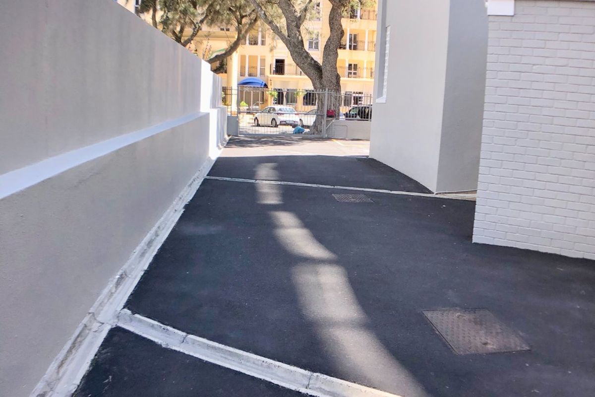 A clean, paved exterior access path between building structures, featuring well-maintained painted brick and concrete boundary walls.