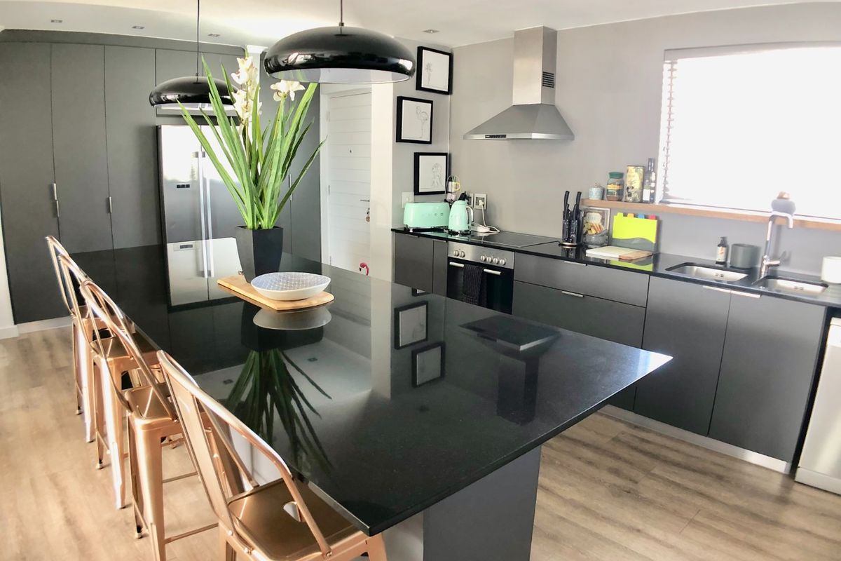 Modern kitchen featuring a large central island with granite countertops, sleek dark cabinetry, integrated appliances, and contemporary recessed lighting.