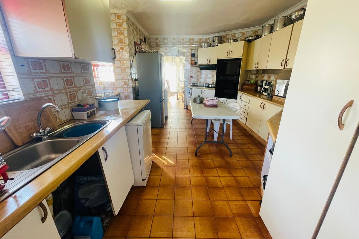 A functional kitchen featuring dated cabinetry, tiled splashbacks, and tiled flooring, offering significant potential for a modern renovation.